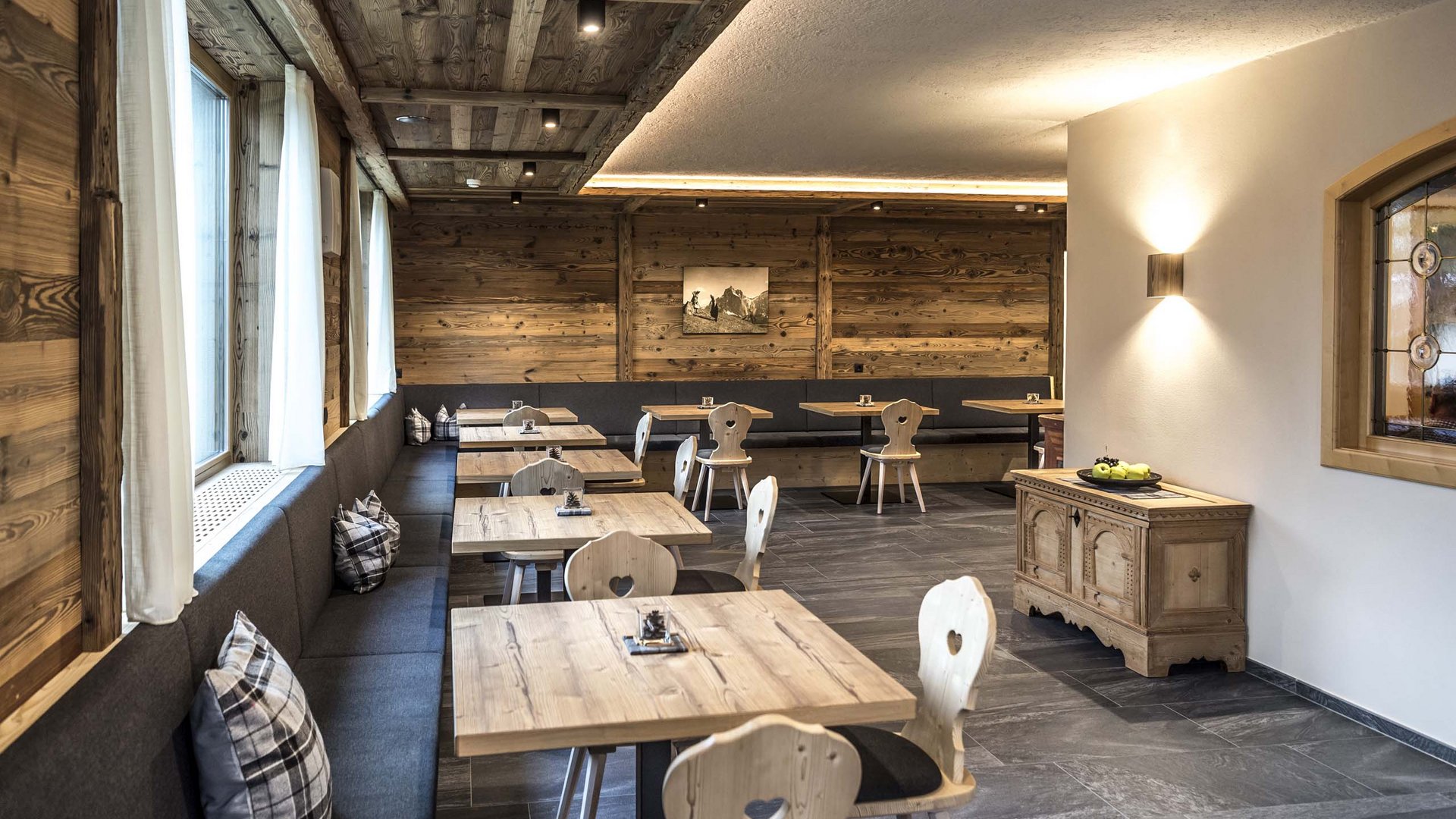 Ab nach Kastelruth, in Ihre Pension mit Frühstück Rustikaler Gastraum mit Holztischen, Stühlen und Kissen auf der Sitzbank